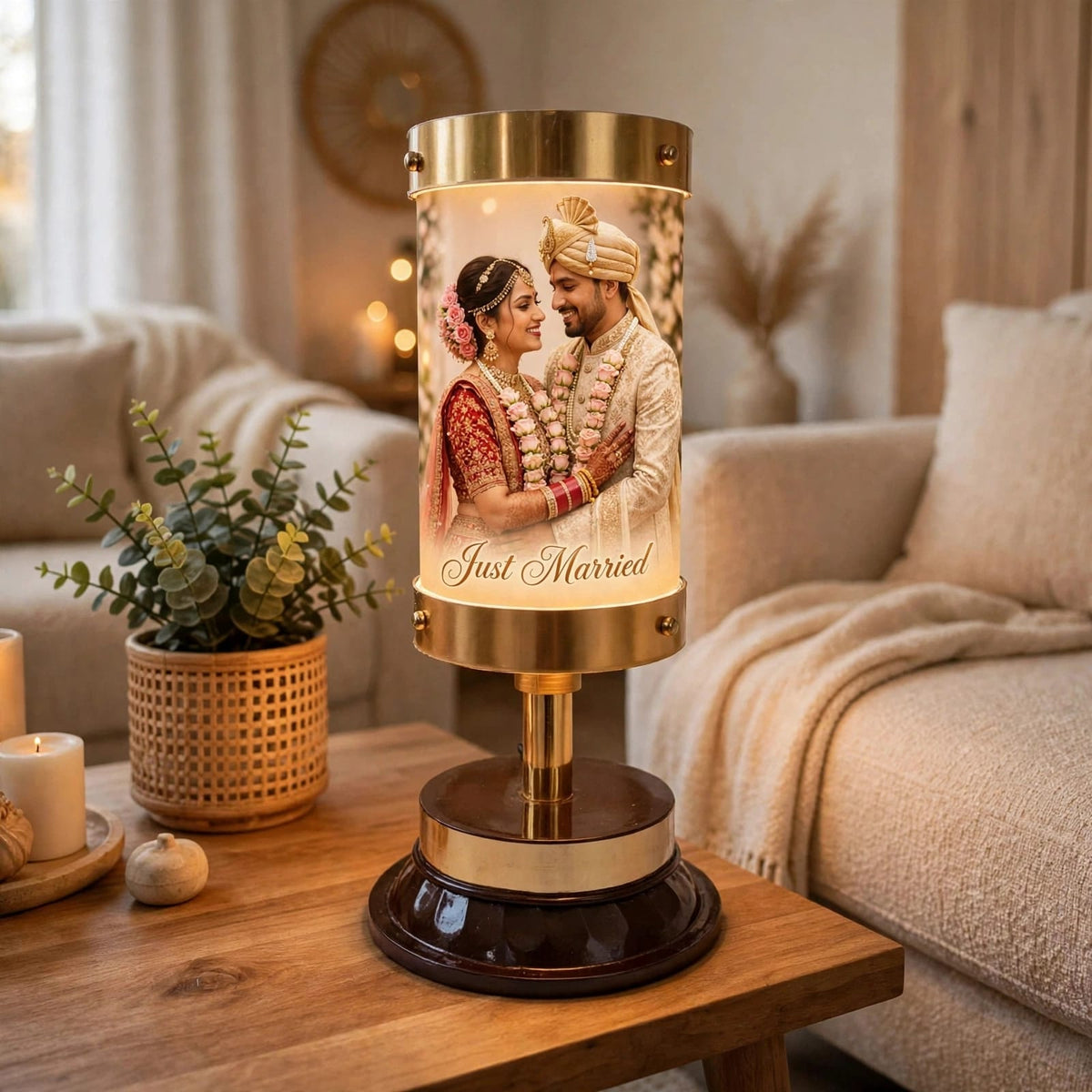 A decorative table lamp with a cylindrical illuminated panel showing a custom wedding photo of a couple and the words 'Just Married,' placed on a wooden table in a cozy living room setting.