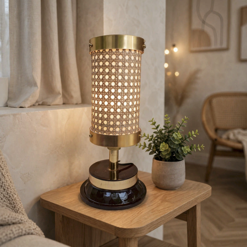 Illuminated rattan cane table lamp with gold trim and a dark base on a wooden side table.