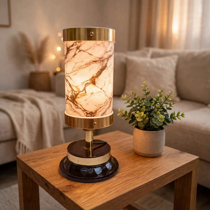 A table lamp with a cylindrical marble-patterned shade and polished brass base, styled on a wooden side table in a cozy living room setting.